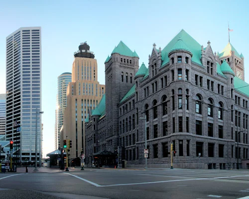 Historisch stadhuis met groene torenspitsen naast moderne wolkenkrabbers op een kruising in Minneapolis