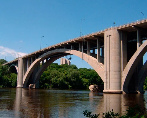 Grote betonnen boogbrug overspant de Mississippi rivier omringd door groene oevers in Minneapolis