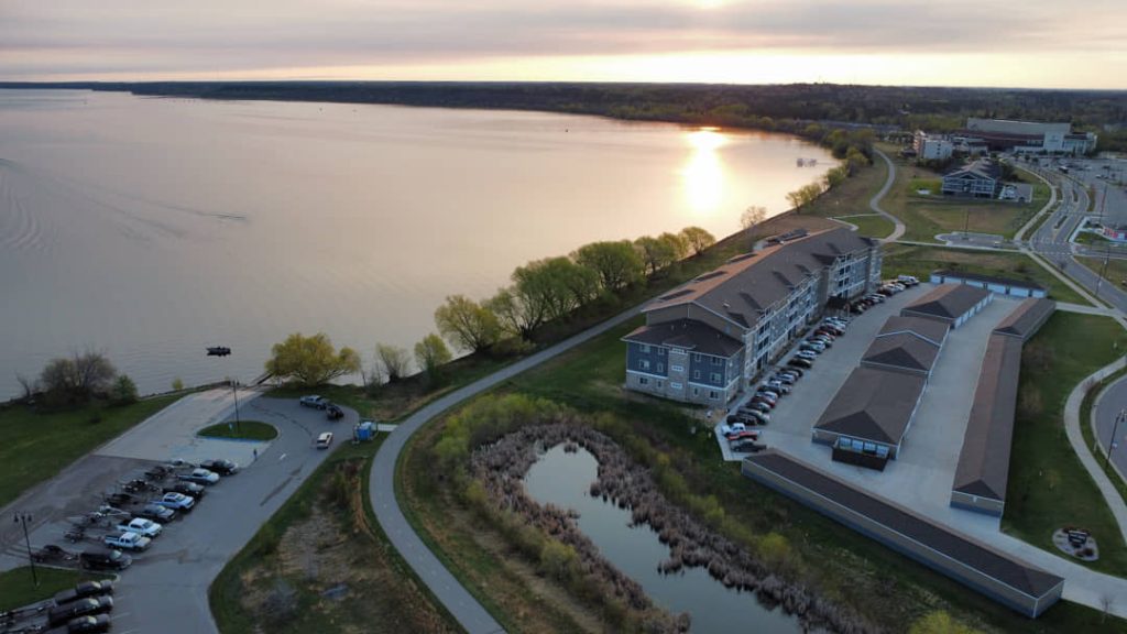Luchtfoto van gebouwen van een resort aan een groot meer, met een vijver op de voorgrond bij zonsondergang