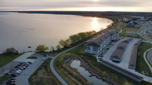 Luchtfoto van gebouwen van een resort aan een groot meer, met een vijver op de voorgrond bij zonsondergang