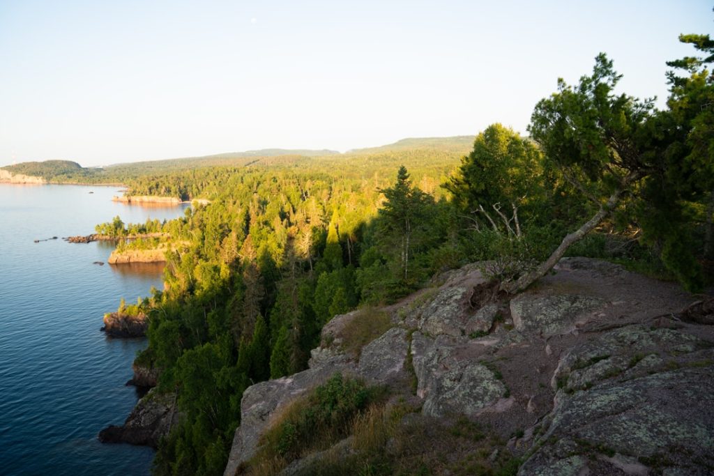 Luchtfoto vanaf een klif over een rotsachtige, beboste kustlijn langs Lake Superior in de avondzon