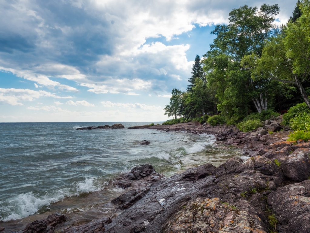 Golven van Lake Superior spoelen over een rotsachtig strand, met bos en struiken langs de oever