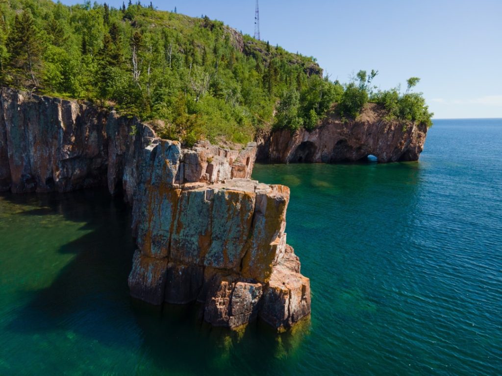 Ruige rotsachtige kliffen bedekt met bos steken uit in het turquoise water van Lake Superior