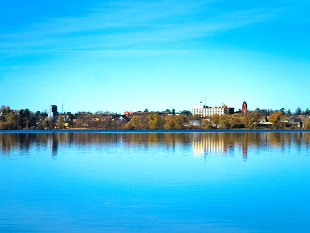 Kleine skyline met een klokkentoren aan de horizon, weerspiegeld in het rustige blauwe water van een meer