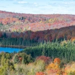 Panoramisch uitzicht over glooiende heuvels met bos in felle herfstkleuren rond een klein blauw meer in Minnesota