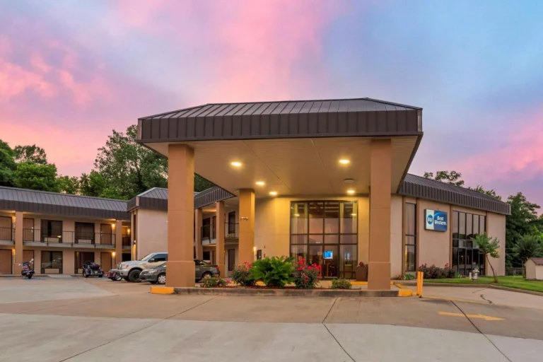Ingang van een Best Western hotel in Mississippi met overdekte oprit en geparkeerde auto's onder een roze avondlucht