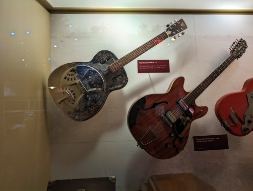 Twee versierde elektrische gitaren hangen tentoongesteld in een glazen vitrine met informatiebordjes in een blues museum in Mississippi