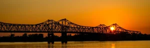 Stalen vakwerkbrug in silhouet over de brede Mississippi rivier met een felle oranje zonsondergang op de achtergrond