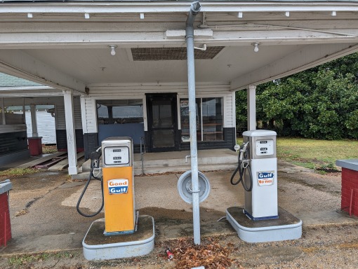 Twee vergeelde oude benzinepompen met het opschrift Gulf voor een leegstaand wit tankstation in Mississippi