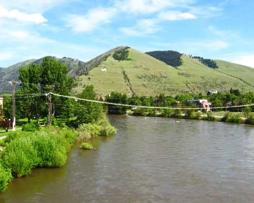Brede rivier stroomt door een vallei met aan de rand van de stad een groene heuvel waarop een grote witte letter M is aangebracht