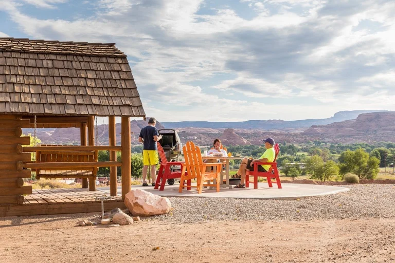 Een groep mensen zit in kleurrijke tuinstoelen bij een houten shelter met uitzicht op rode rotsformaties bij Moab, Utah