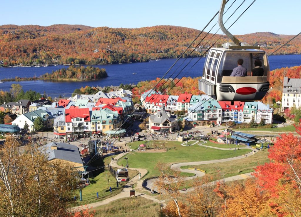 Gondellift zweeft over het kleurrijke bergdorp van Mont-Tremblant met felgekleurde herfstbossen en een meer op de achtergrond