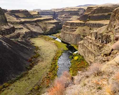 Smalle rivier kronkelt door een diepe kloof met gelaagde rotswanden en droog struikgewas op de randen