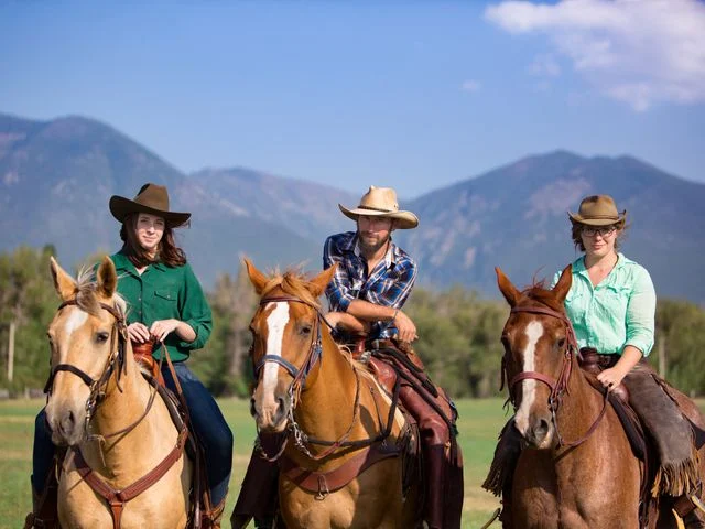 Drie ruiters op paarden poseren op een grasveld met bergen op de achtergrond op een ranch in Montana