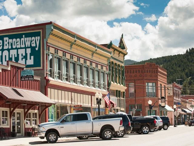 Historische bakstenen gebouwen met een hotel en geparkeerde pick-uptrucks langs de hoofdstraat van een klein stadje in Montana