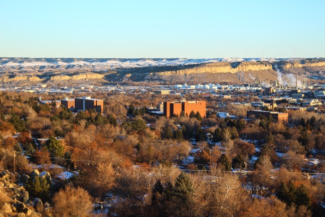 Luchtfoto van de stad Billings in de winter met kale bomen, gebouwen en een hoge rotswand met fabrieksschoorstenen op de achtergrond