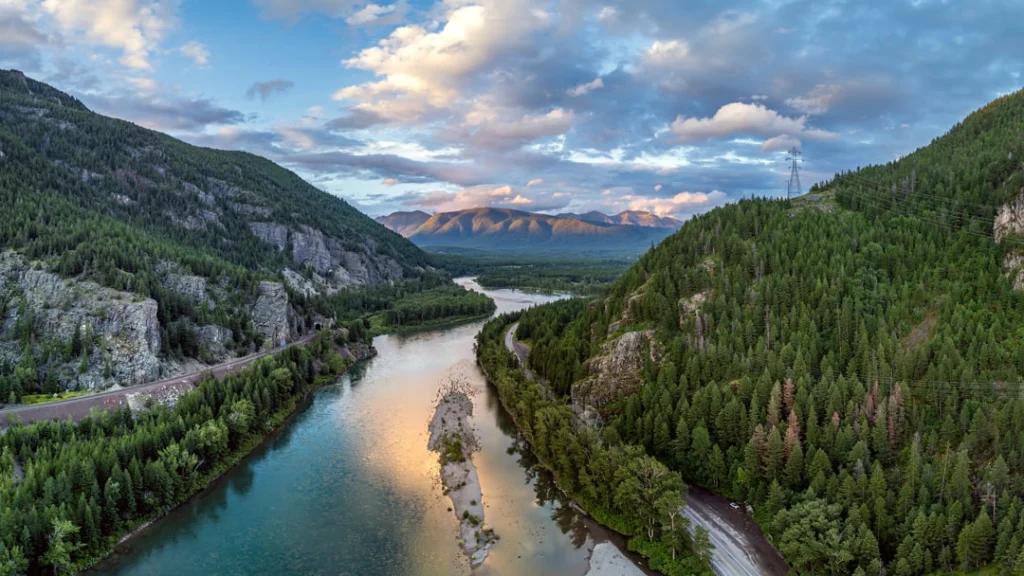 Luchtfoto van een blauwe rivier die kronkelt door een dal tussen beboste bergen bij zonsondergang