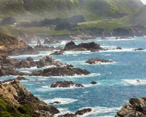 Rotsachtige kustlijn met schuimende golven en groene heuvels langs de kust bij Monterey in Californie