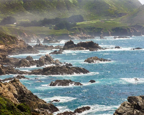 Rotsachtige kustlijn met schuimende golven en groene heuvels langs de kust bij Monterey in Californie