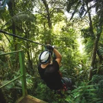 Een man met helm glijdt aan een zipline door het dichte groene regenwoud van Monteverde tijdens een canopy tour