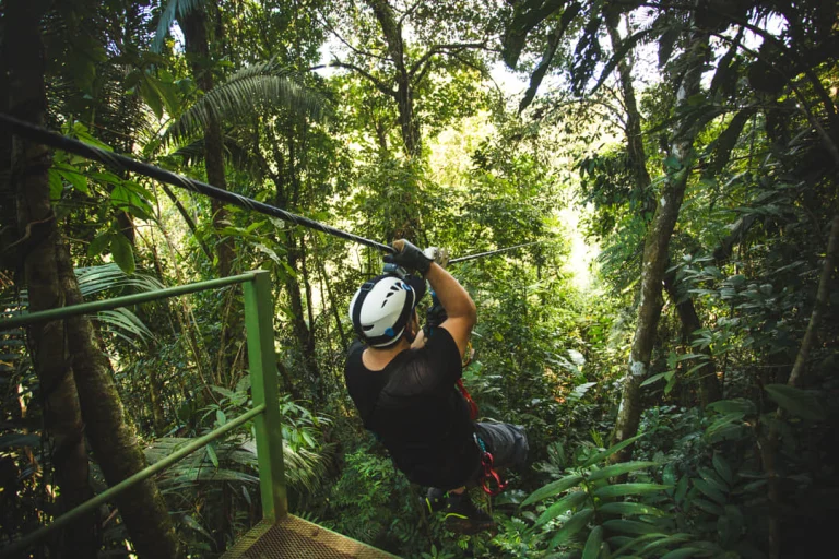 Een man met helm glijdt aan een zipline door het dichte groene regenwoud van Monteverde tijdens een canopy tour