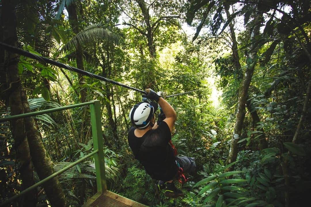 Een man met helm glijdt aan een zipline door het dichte groene regenwoud van Monteverde tijdens een canopy tour