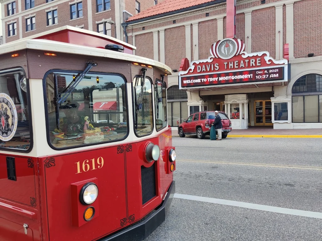 Rode toeristische trolleybus stopt op straat voor de verlichte gevel en luifel van het Davis Theatre in Montgomery in Alabama