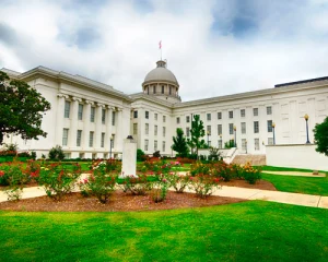 Wit classicistisch capitoolgebouw met koepel in Montgomery in Alabama, gezien over een tuin met rozenstruiken en grasvelden