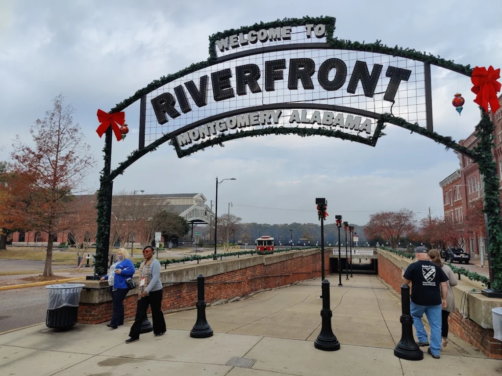 Versierde metalen welkomstboog met de tekst welkom bij riverfront montgomery alabama boven een wandelpad met wandelaars