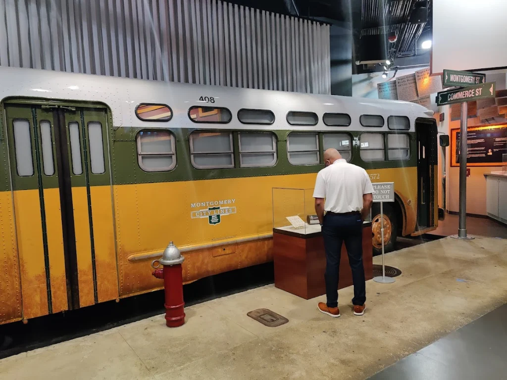 Man bekijkt een vitrine naast een oude groen-gele stadsbus van Montgomery City Lines in een museum