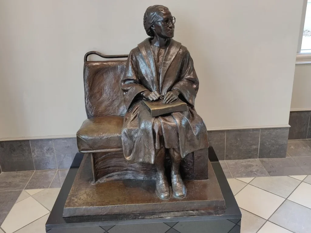 Bronzen standbeeld van een zittende vrouw met bril op een bankje, ter herdenking van Rosa Parks in Montgomery