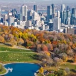 Luchtfoto van een uitgestrekt herfstpark met een vijver, wandelaars en de wolkenkrabbers van Montreal op de achtergrond