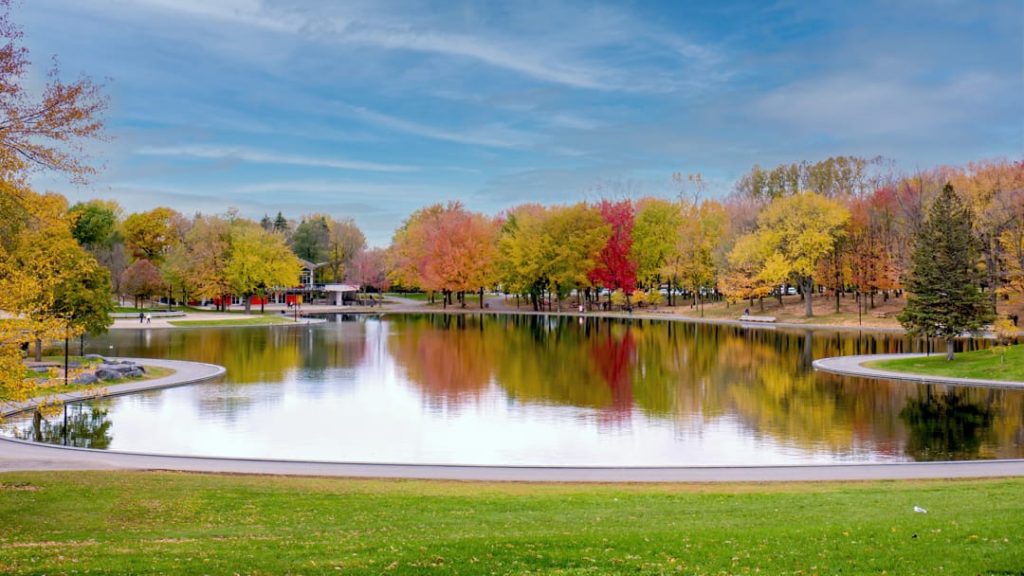 Rustige vijver met een grasrand, omringd door bomen in geel en rood herfstkleuren met een paviljoen aan de overkant