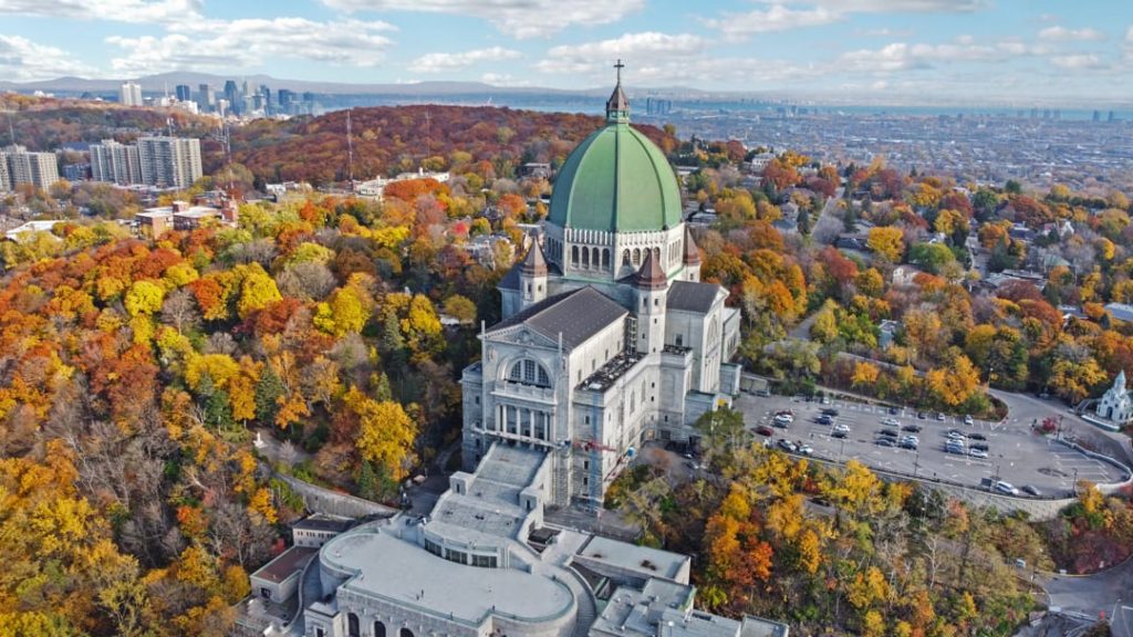 Luchtfoto van het Sint-Jozefsoratorium met groene koepel omringd door herfstbladeren in Montréal, met de skyline op de achtergrond