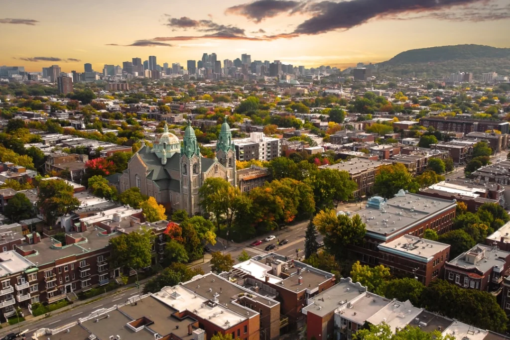 Wolkenkrabbers van het centrum van Montréal steken uit boven een woonwijk met een kerktoren op de voorgrond bij zonsondergang