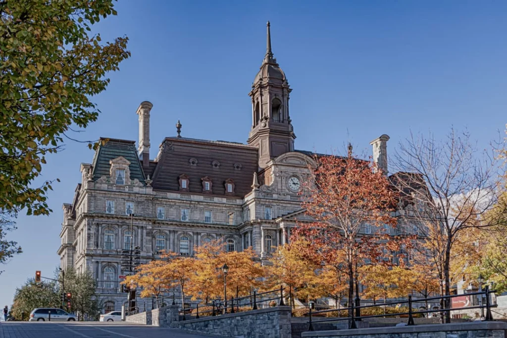 Statig stadhuis van Montreal met een koepeltoren, gefotografeerd tussen felgekleurde herfstbomen onder een strakblauwe hemel