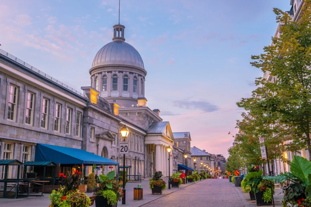 Verlichte straat met terrassen en bloembakken langs de koepel van de Bonsecours markt in Montréal bij zonsondergang