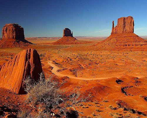 Vier rode rotsformaties verspreid over de vlakte van Monument Valley met een zandpad dat er tussendoor slingert