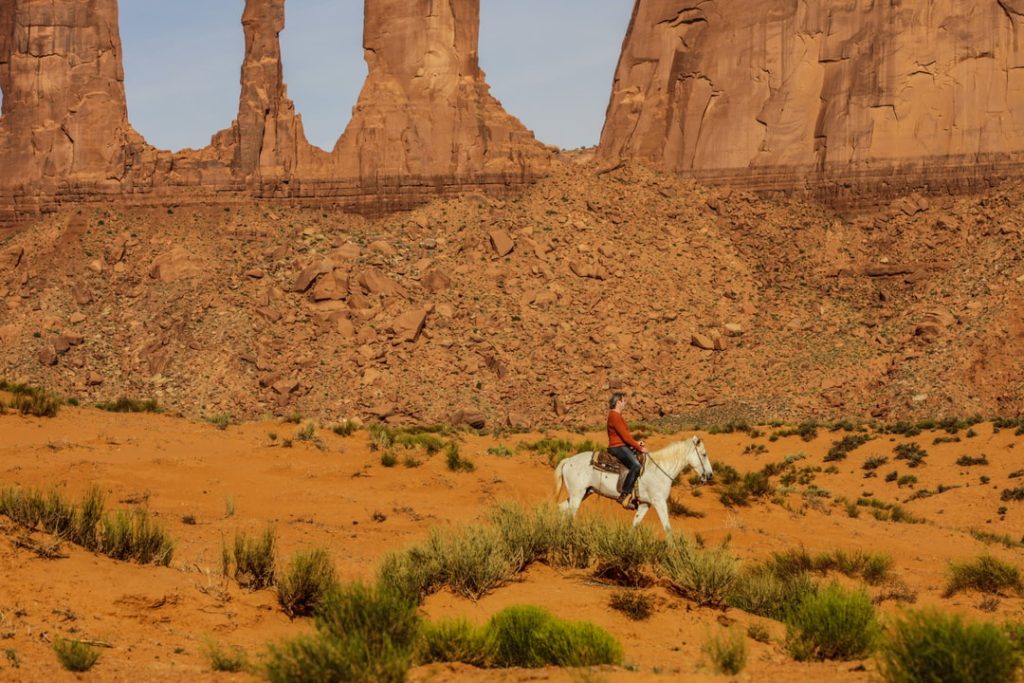 Een ruiter te paard rijdt door de rossige woestijn van Monument Valley met hoge rotsformaties op de achtergrond