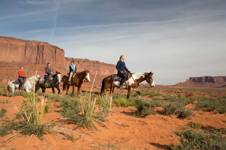 Vier ruiters te paard rijden door de rode woestijn van Monument Valley met indrukwekkende rotsformaties op de achtergrond