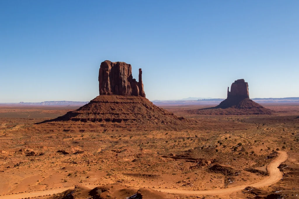De karakteristieke rode rotsformaties van Monument Valley steken hoog boven de dorre woestijnvlakte uit onder een strakblauwe hemel
