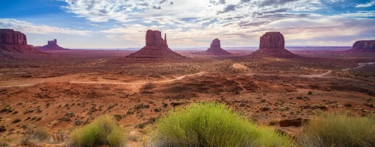 Uitzicht over de rode woestijnvlakte van Monument Valley met de kenmerkende torenhoge rotsformaties onder een bewolkte lucht