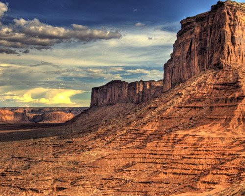 Hoog rotsplateau met steile wanden en een lager gelegen mesa in de rode woestijn van Monument Valley bij avondlicht