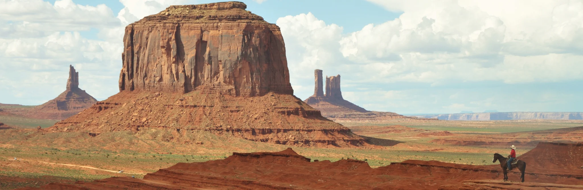 Eenzame ruiter te paard kijkt uit over de rode rotsformaties en mesa's van Monument Valley onder een bewolkte lucht