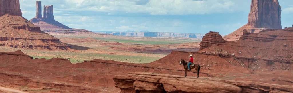 Een ruiter te paard staat op een rotsplateau met uitzicht over de rode rotsformaties van Monument Valley in het westen van Amerika