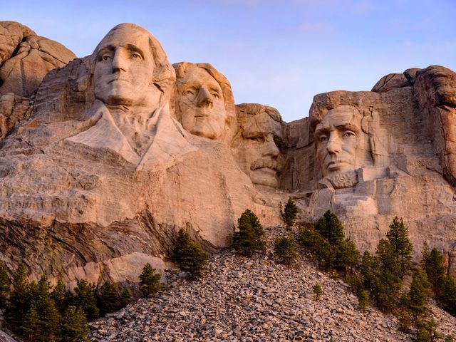 De vier reusachtige presidentenkoppen uitgehouwen in de rotswand van Mount Rushmore in South Dakota met dennenbomen op de voorgrond