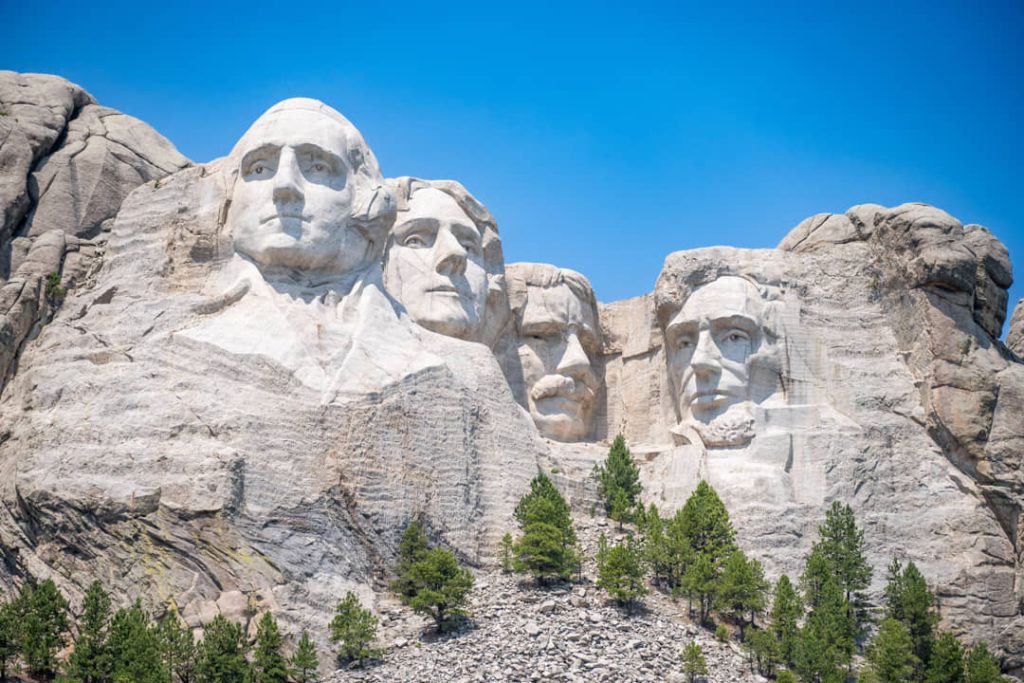 De uitgehouwen gezichten van vier Amerikaanse presidenten in de rotswand van Mount Rushmore onder een strakblauwe lucht