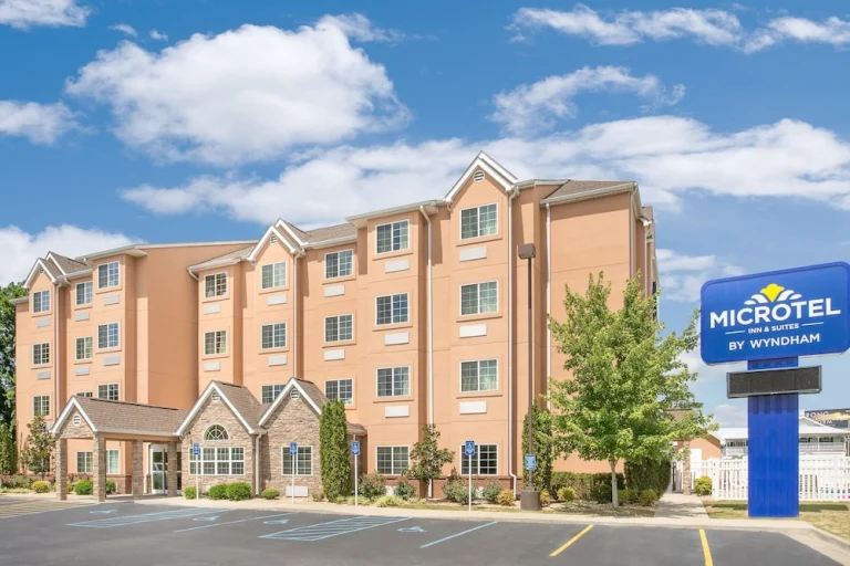 Gevel van het hotel Microtel Inn & Suites by Wyndham in Muscle Shoals met parkeerterrein en blauw uithangbord op een zonnige dag
