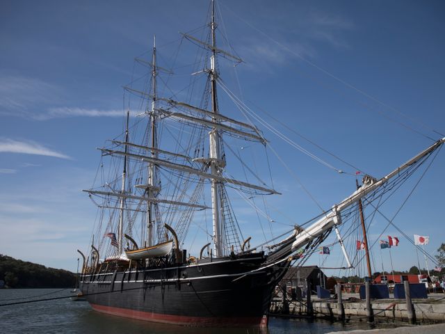 Zwart houten driemaster zeilschip met hoge masten afgemeerd aan de kade van Mystic Seaport in Connecticut onder een blauwe lucht