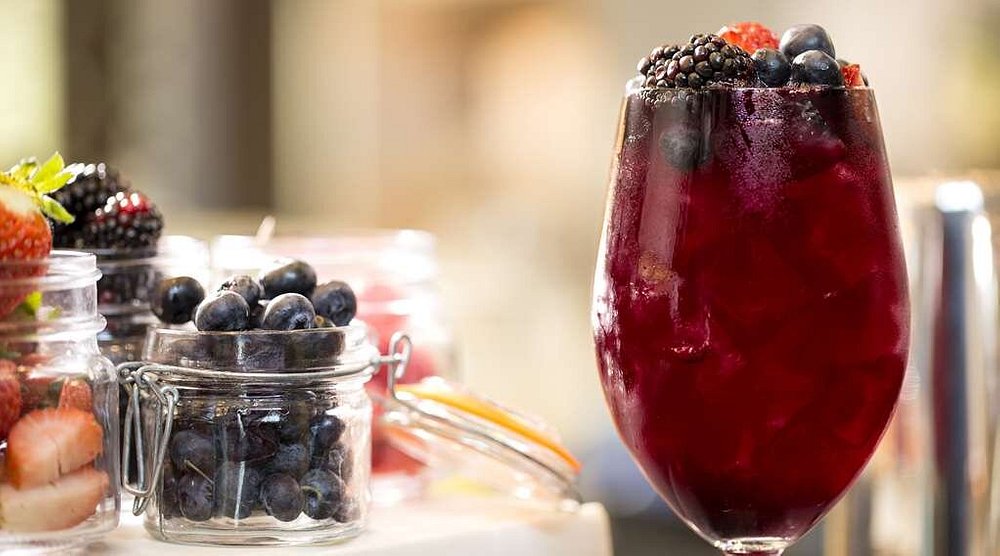 Donkerrode sangria met bramen en bosbessen in een groot glas staat naast potjes met aardbeien en bosbessen